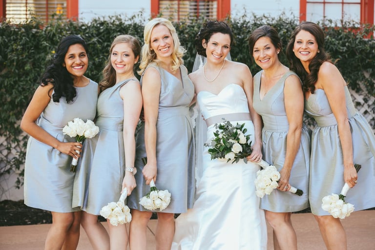 Bride in strapless gown with bridesmaids in silver dresses, showcasing elegant down hairstyles and holding white bouquets.