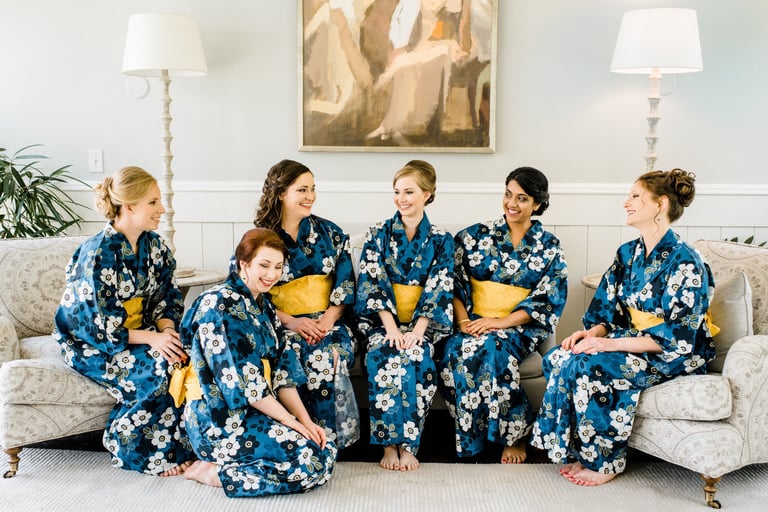 Bride and bridesmaids in matching floral robes with styled hair and soft makeup share a joyful moment before the wedding.