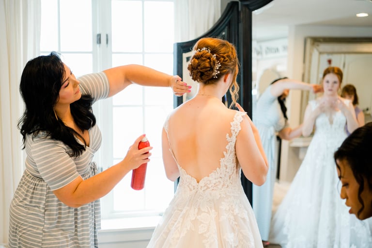 Stylist sprays the bride’s elegant updo with pearls as she prepares in a lace gown with bridal makeup before the ceremony.