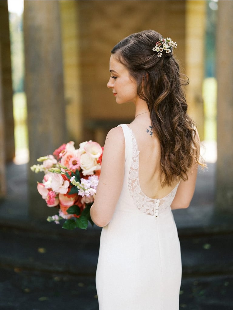 Bride with half up half down hairstyle and floral hairpiece, holding bouquet while wearing lace back wedding gown.