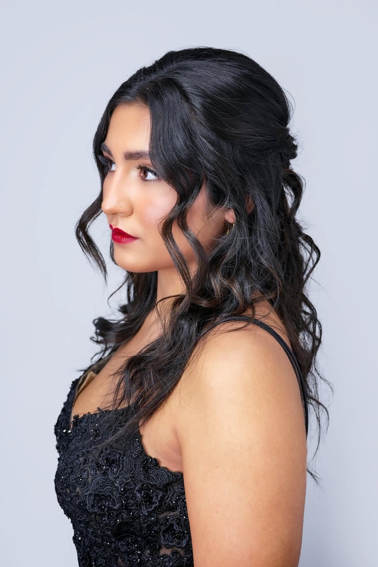 Woman with dark hair in half up hairstyle with loose curls and face framing tendrils, wearing black dress and red lipstick.