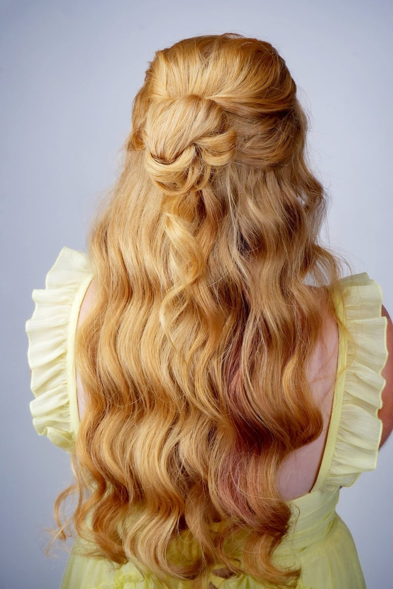 Woman with long red-blonde hair in half up half down waves with twisted knot detail, romantic hairstyle for wedding or event.