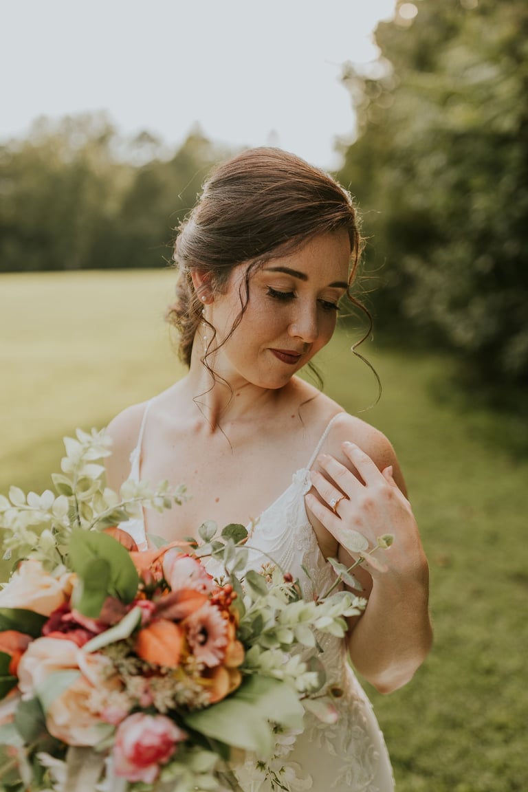 Bride with romantic wedding makeup and soft updo hairstyle holding colorful bouquet, captured outdoors in natural light.