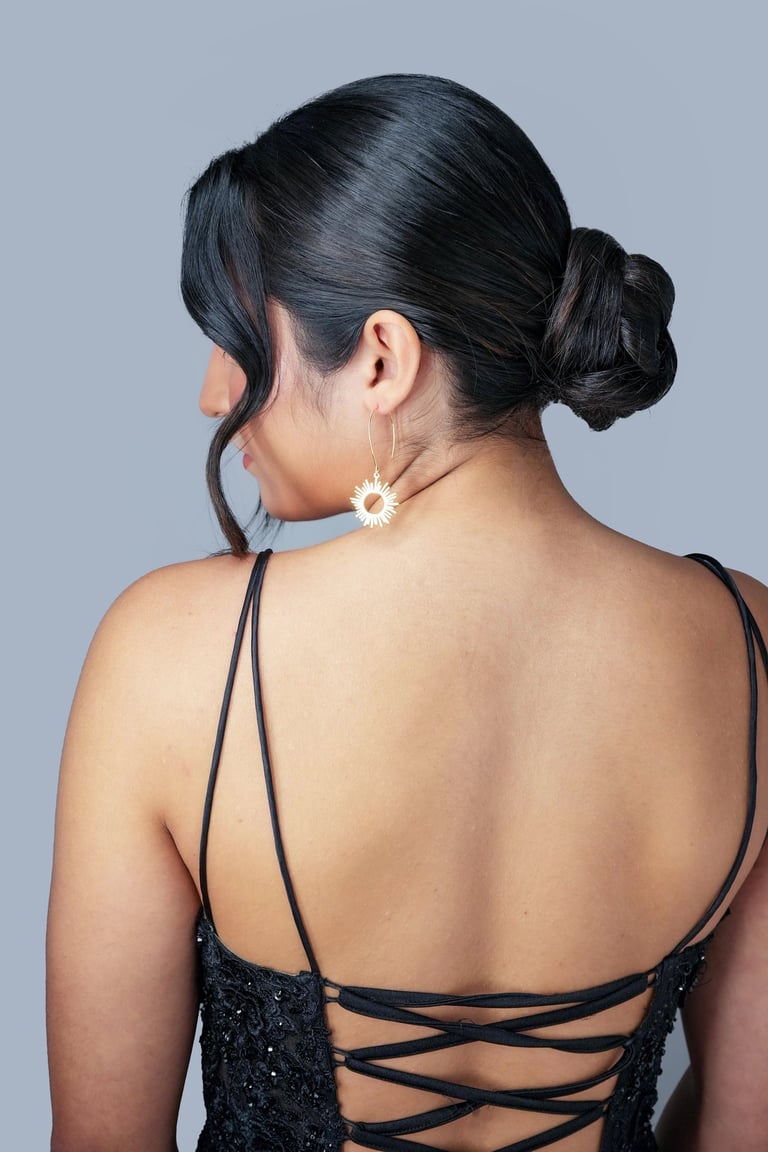 Bride with sleek low bun updo wearing black strappy dress and gold sun earrings, elegant hairstyle for formal event.