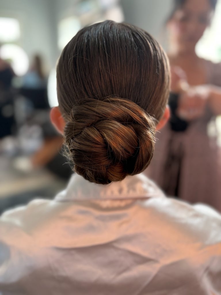Bride with sleek twisted low bun hairstyle wearing white robe, elegant polished look while getting ready on wedding morning.