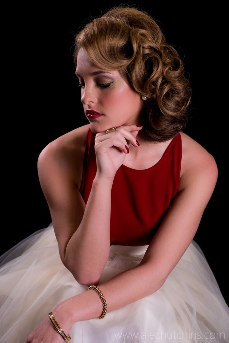 Woman with vintage curled hairstyle, red lipstick and gold eyeshadow wearing red top and white skirt, retro glamour look.