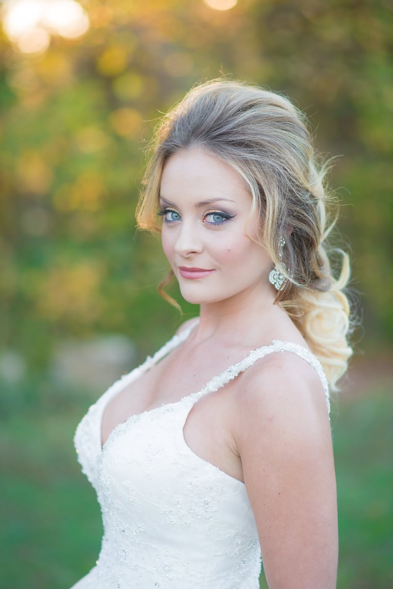 Bride with half-up bridal hairstyle, natural wedding makeup, winged eyeliner, glowing skin, and jeweled earrings outdoors.