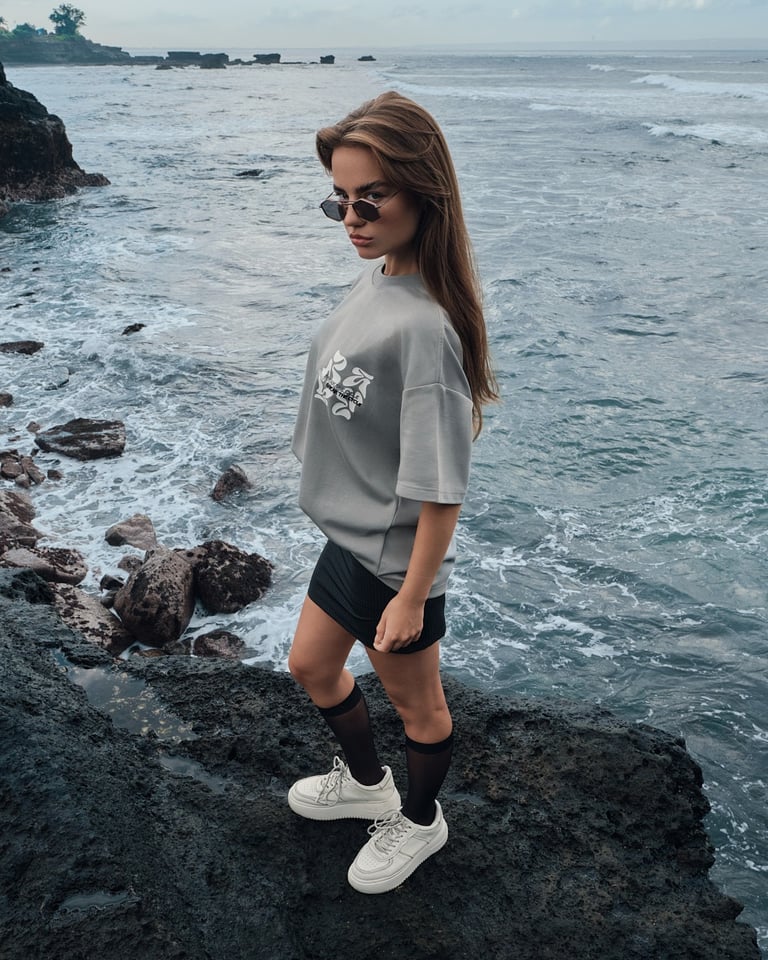 Model in an oversized shirt and mini skirt poses in a preppy street style on Bali’s volcanic coast.