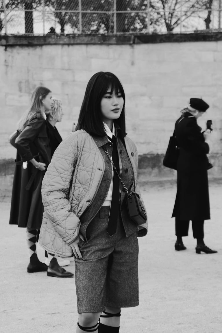 une femme à la fashion week qui porte un bermuda des vestes superposées et une cravate