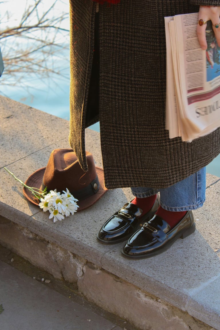 une femme qui porte des mocassins en cuir nois, des chaussettes rouges un jean bleu et un pardessus prince de galles