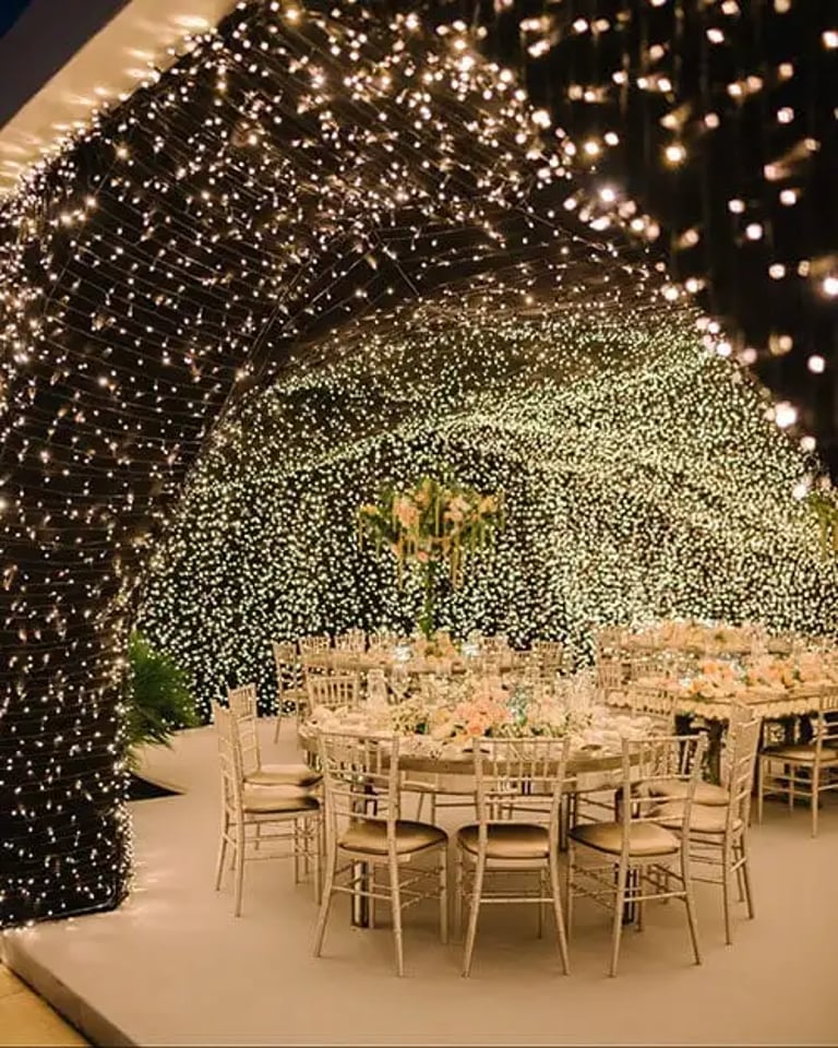 Elegant outdoor wedding reception with round tables under a canopy of twinkling fairy lights.