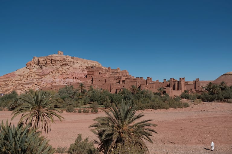 Città marocchina di Hait Ben Haddou con palme, persona vestita in bianco e cielo azzurro