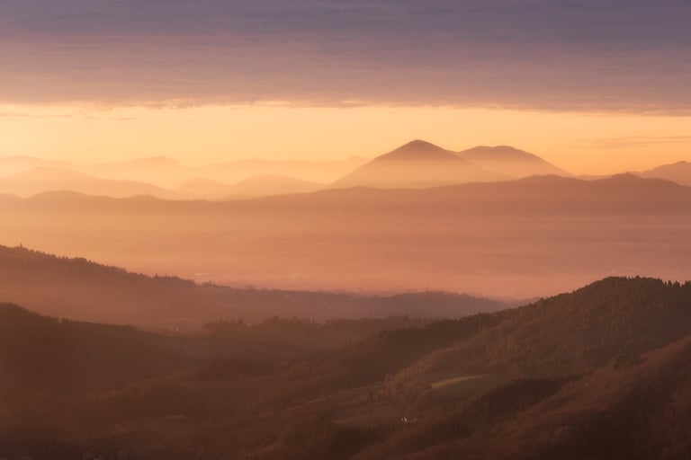 Colori caldi dell'alba che illumina la nebbia mattutina con colline sullo sfondo