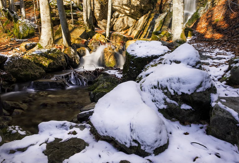 neve su sassi con fiume e colori autunnali sullo sfondo