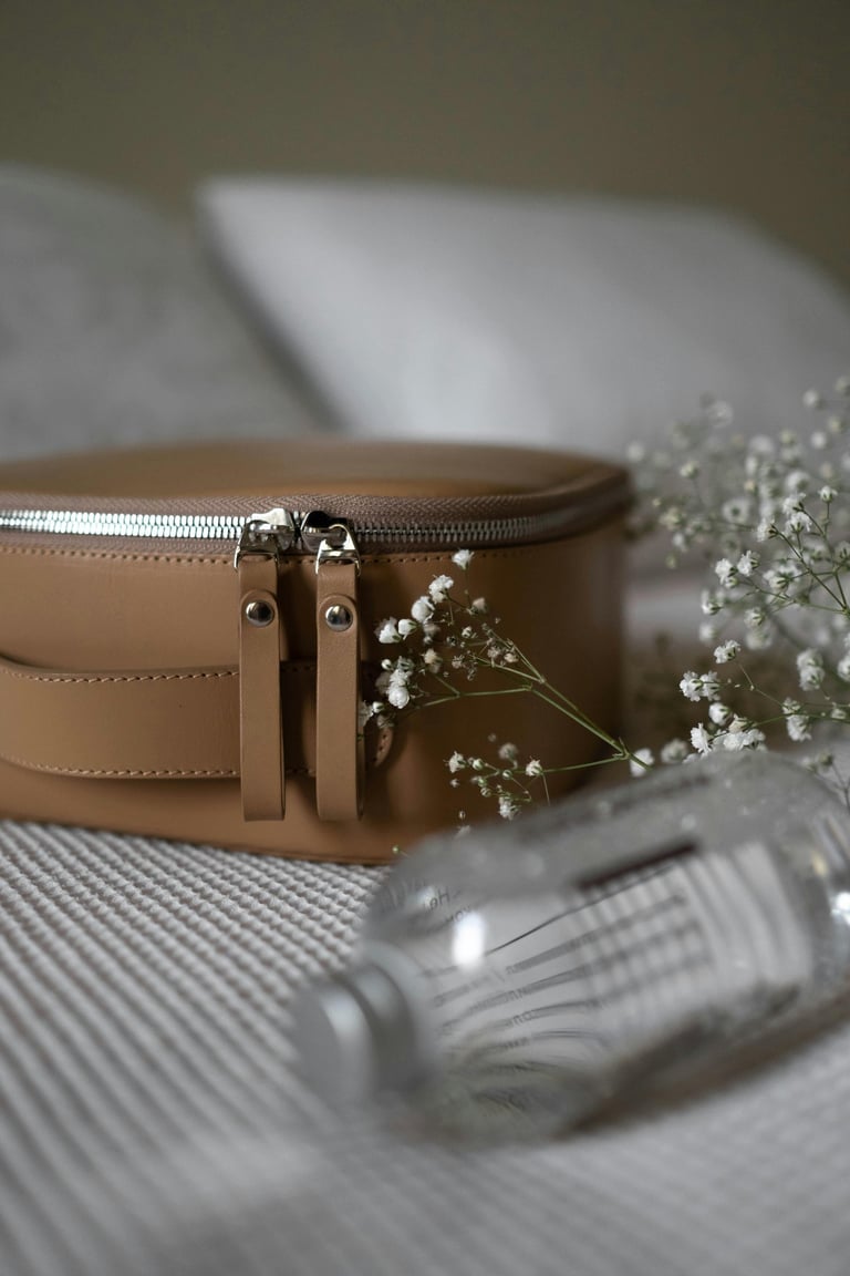 Elegant tan leather travel makeup bag with silver zippers beside white baby's breath flowers.