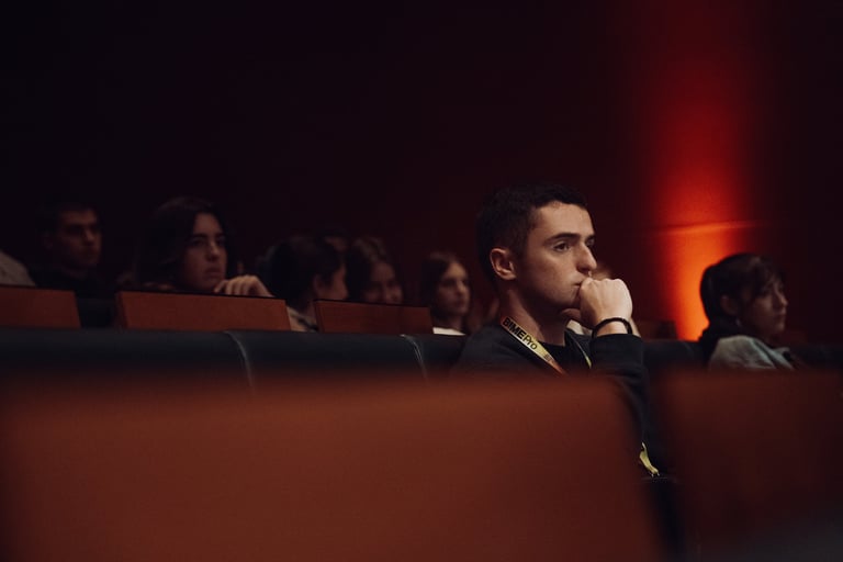 Young man with a BIME lanyard attentively watching a presentation at BIME Bilbao. Seated in a dark auditorium with other atte