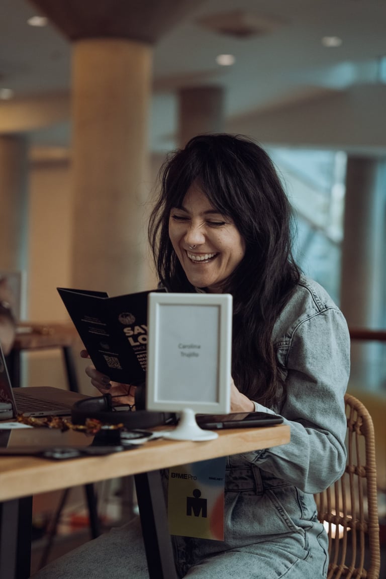 Smiling woman with a BIME Bilbao lanyard reading a program at a table with a name card. Enjoying the event in Bilbao