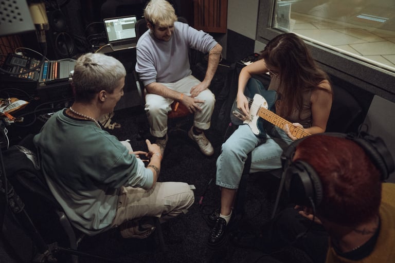 Musicians collaborating in a studio at BIME Bilbao. Woman playing electric guitar, two men listening. Laptop and equipment vi