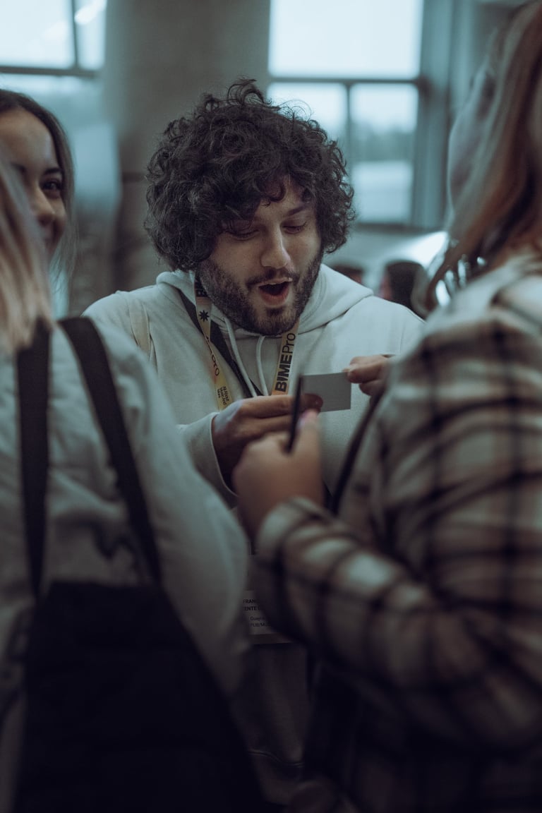 Man with curly hair wearing a BIME Pro lanyard exchanging business cards with two other attendees at BIME Bilbao. Networking 