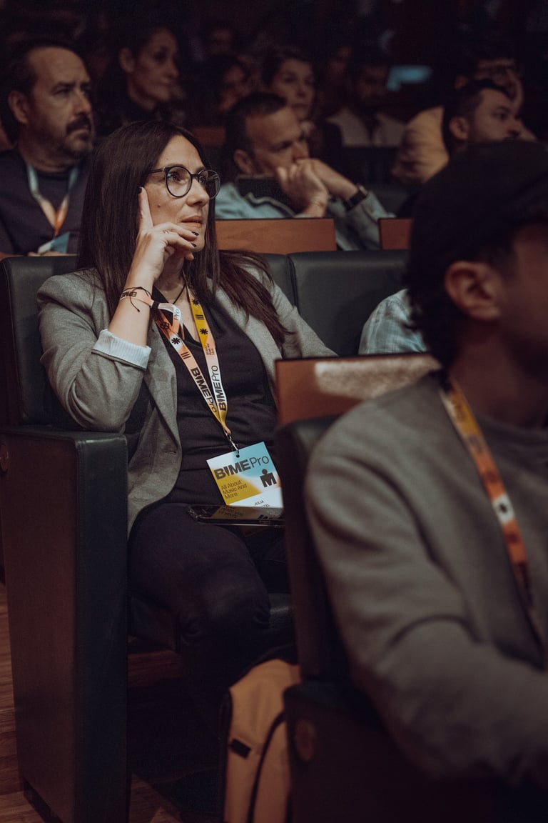 Woman with glasses wearing a BIME Pro lanyard attentively listening in an audience at BIME Bilbao. Conference or panel sessio