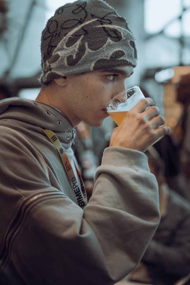 Young man with a BIME Pro lanyard and a patterned beanie drinking a glass of beer at BIME Bilbao. Casual moment at the event