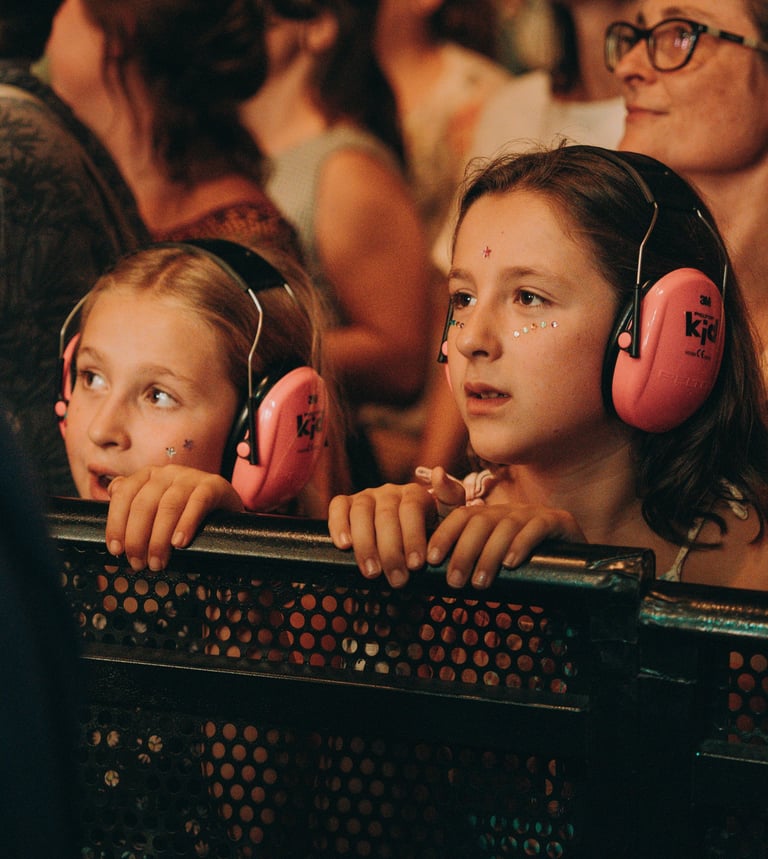 Two young girls wearing pink ear protectors watch a performance at SONORAMA RIBERA in Bilbao. Music festival audience