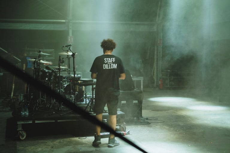 Dillom's staff member in a t-shirt stands near a drum kit on stage at SONORAMA RIBERA in Bilbao. Music festival backstage