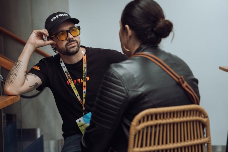 Man with a BIME Pro lanyard and yellow sunglasses talking to a woman at BIME Bilbao. Casual conversation during the event