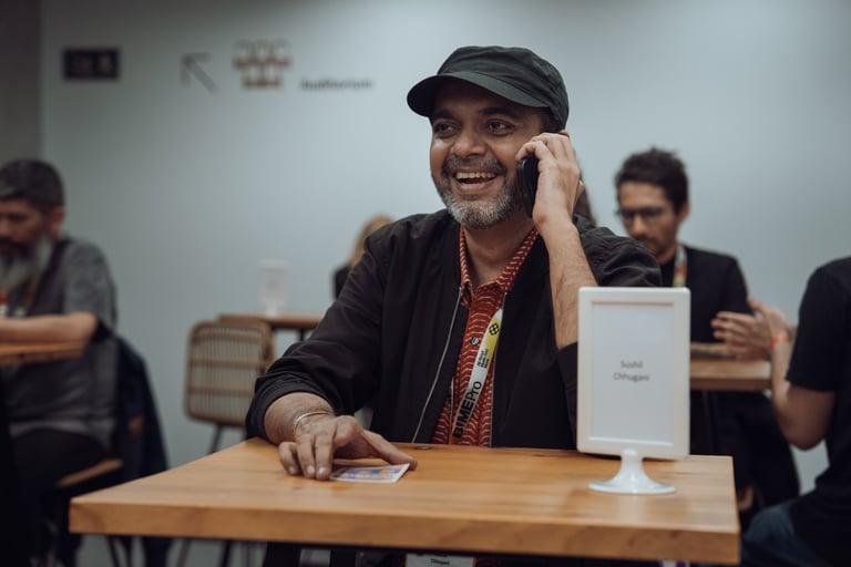 Smiling man with a BIME Pro lanyard talking on his phone at a table during BIME Bilbao. Indoor networking space