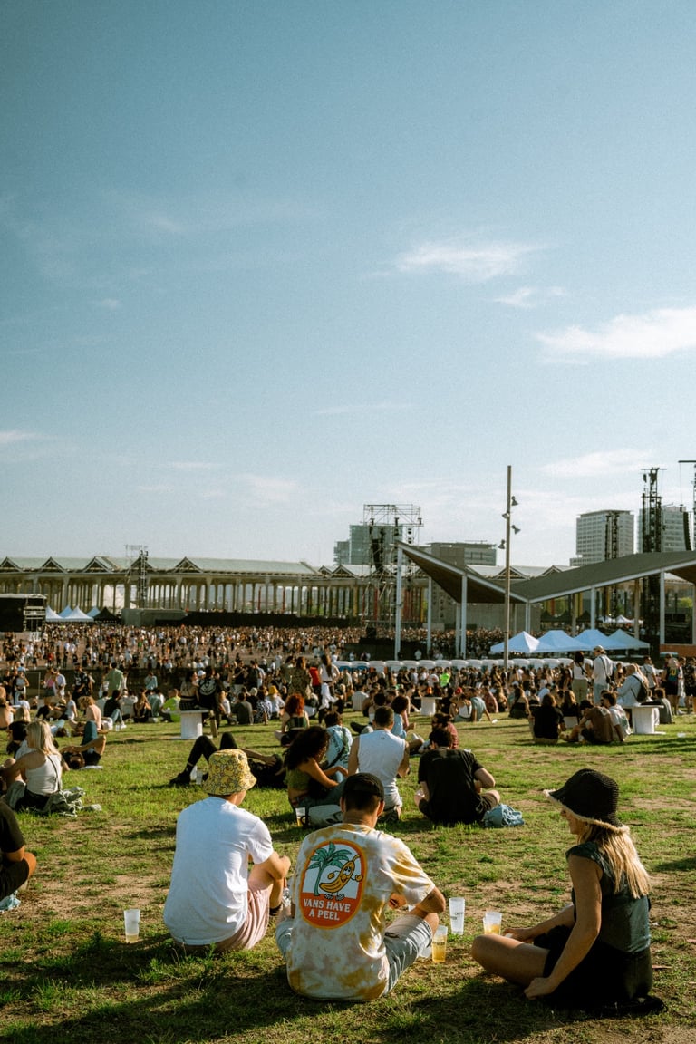 Large crowd relaxing on the grass at an outdoor festival in Bilbao, Basque Country, Spain. Stage in the distance under a clea