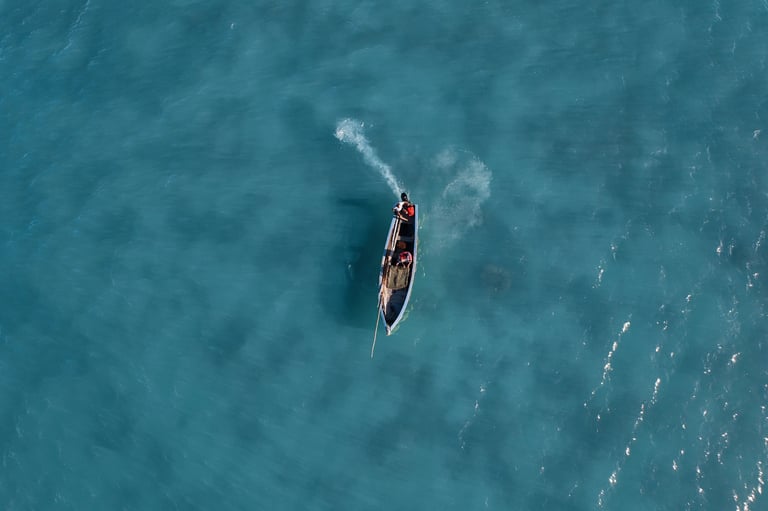 Location: Anse La Raie. Aerial view of a boat gliding across the clear blue waters of Mauritius, with two fishermen onboard