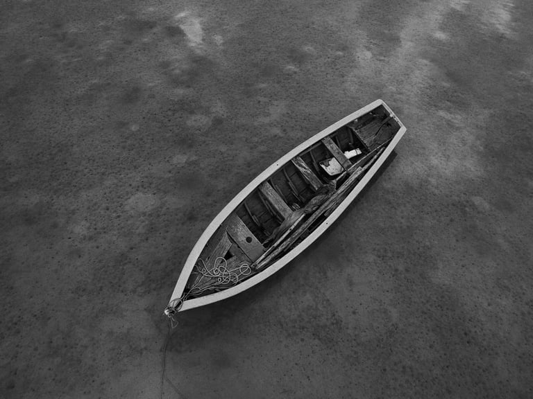 Location: Butte a L'herbe. Black and white aerial view of a solitary wooden boat floating on calm waters in Mauritius