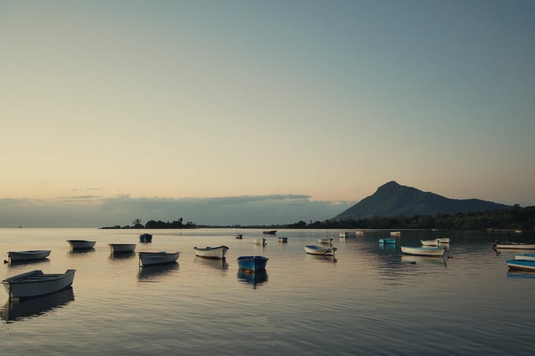 Serene view of boats anchored on a calm sea at sunset in Petite Case Noyale, Mauritius, with mountains in the background