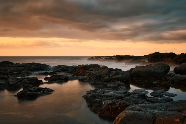 Long exposure shot of rocky shoreline at sunset in Albion, Mauritius, with dramatic clouds over the ocean