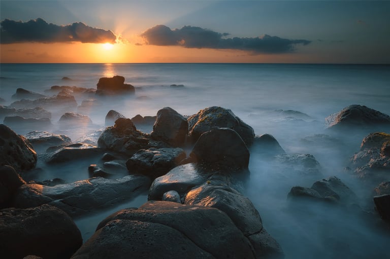 Sunset over ocean rocks in Albion, Mauritius, with long exposure waves creating misty effects