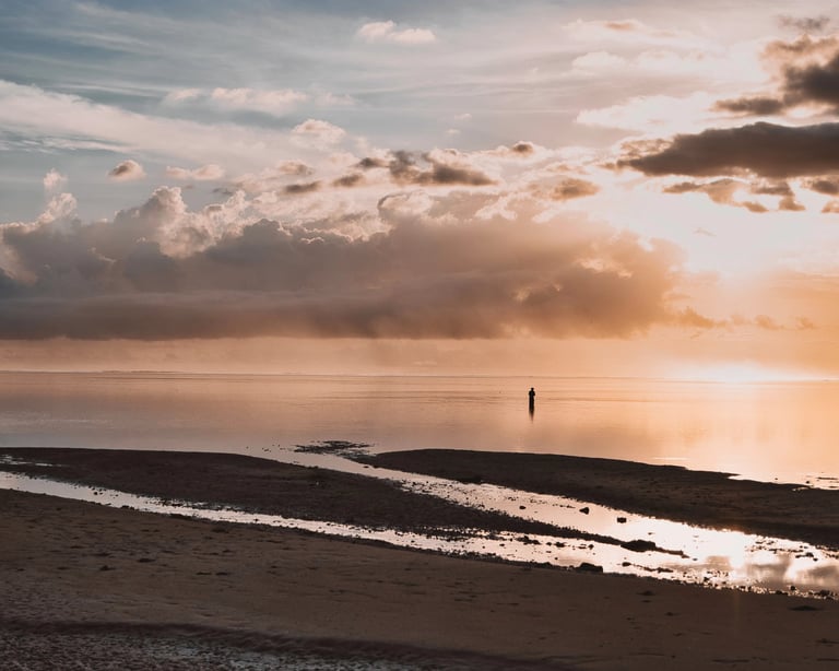 Lone figure standing in shallow water during a peaceful sunrise at la Prairie beach in Mauritius, with dramatic clouds