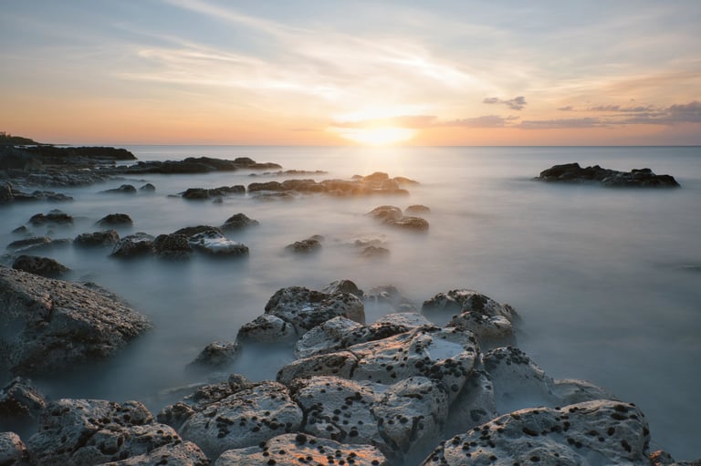 Calm ocean waters at sunset washing over rocky shores in Mauritius, with soft light illuminating the rugged coastline