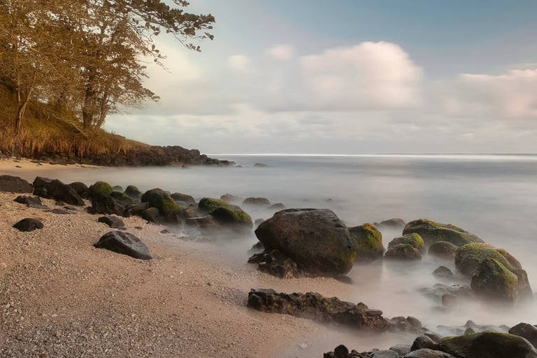Peaceful morning on a secluded Souillac beach in Mauritius, with moss-covered rocks and soft waves gently washing ashore