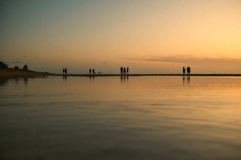 Silhouettes of people walking along the shoreline at sunset in La Prairie, Mauritius, with calm waters reflecting golden hues