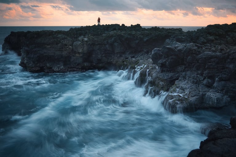 Waves crashing against rocky cliffs at sunset in Le Souffleur, Mauritius, with silhouetted figures on the coast