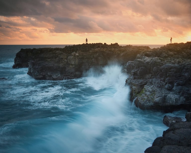 Waves crashing against rocky cliffs at sunset in Le Souffleur, Mauritius, with silhouetted figures on the coast
