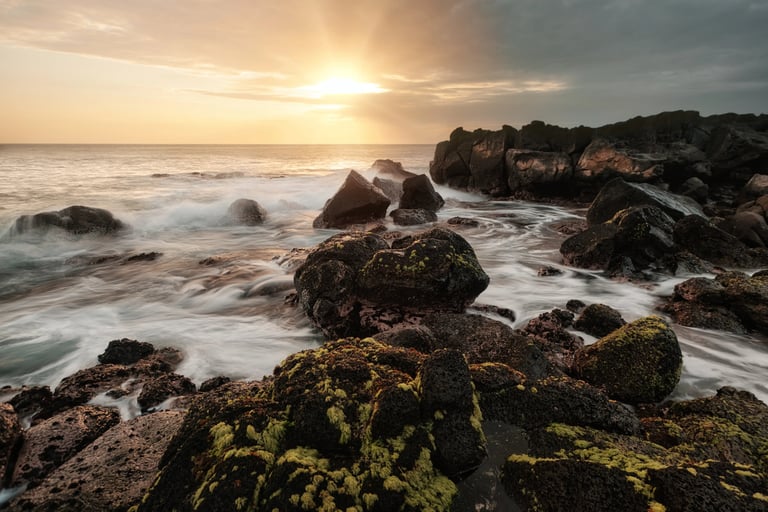 Sunset over moss-covered rocks along the rugged coastline of Albion, Mauritius, with waves gently crashing against the shore