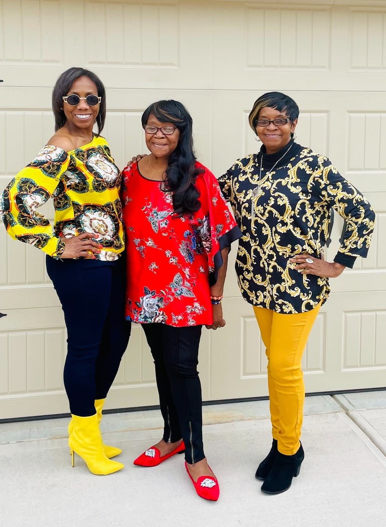 Three fashionable women posing in vibrant patterned tops and colorful boots in front of a garage door.