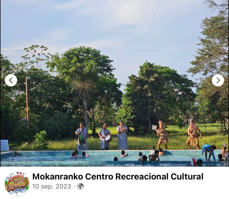 Indigenous performers dancing and drumming for people in a swimming pool at Mokanranko Centro Recreacional.