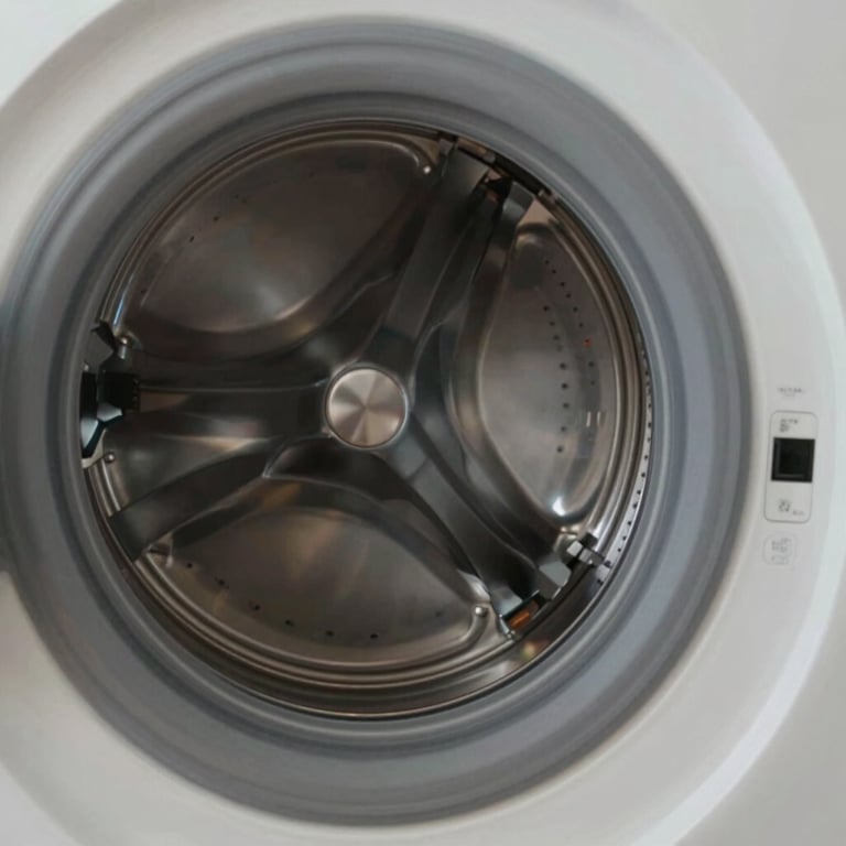 A close-up of a high-efficiency washing machine's drum being inspected by a professional in a Middle Eastern / Gulf apartment, soft lighting, clean and professional.