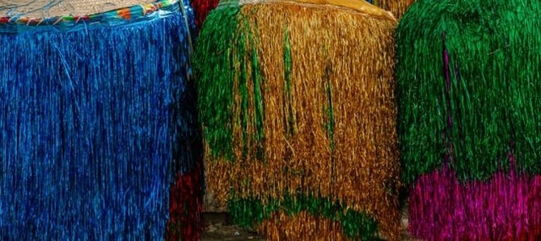 Foto de três estruturas cilíndricas com franjas metálicas coloridas lado a lado.