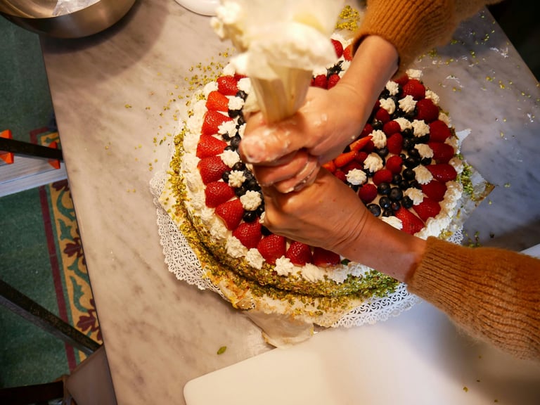 aplicando betún blanco con manga pastelera sobre una tarta de frutas decorada con fresas y arándanos