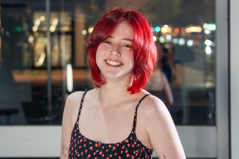 Smiling young woman with vibrant red hair wearing a floral dress against a city bokeh background.