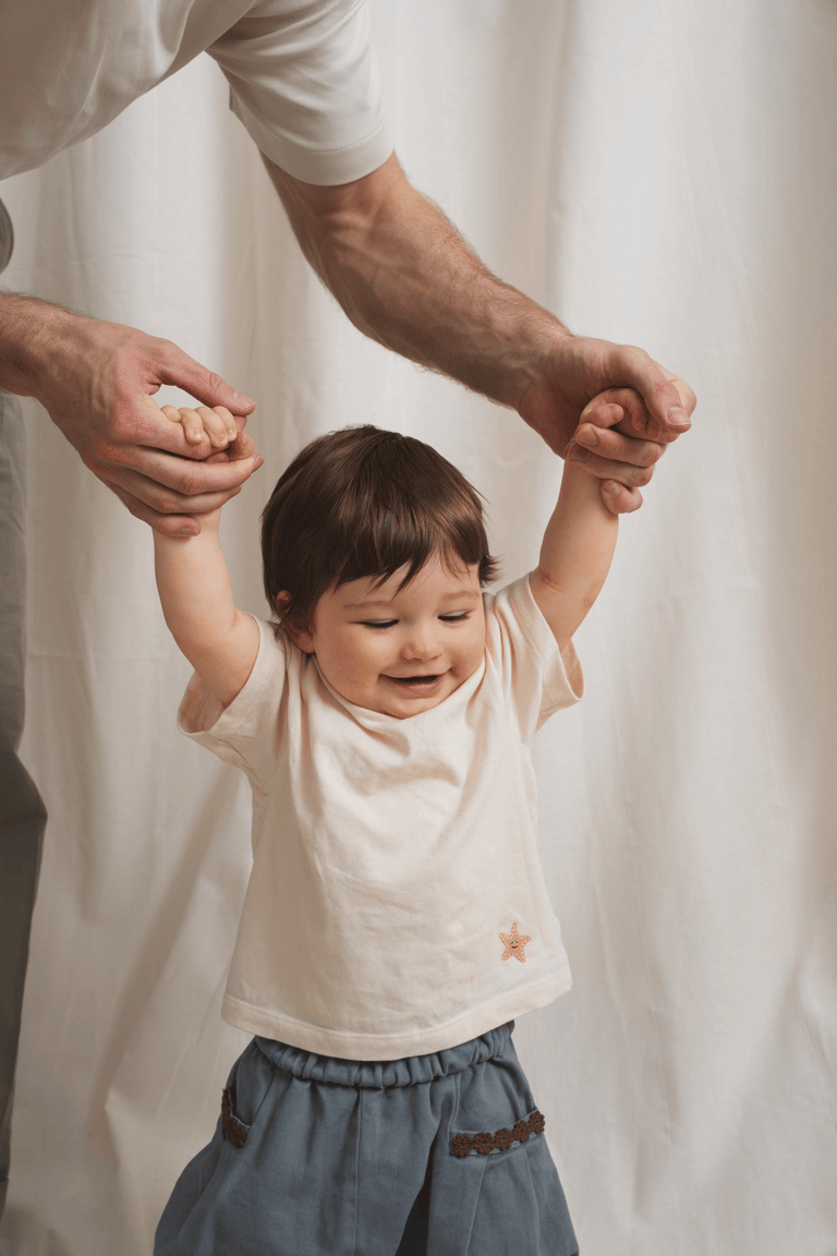 Dad holding hands of baby trying to stand. Studio setting, soft light.