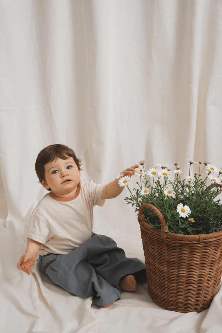 Baby sitting in a studio setting, touching flower pot. Soft studio light and textile background.